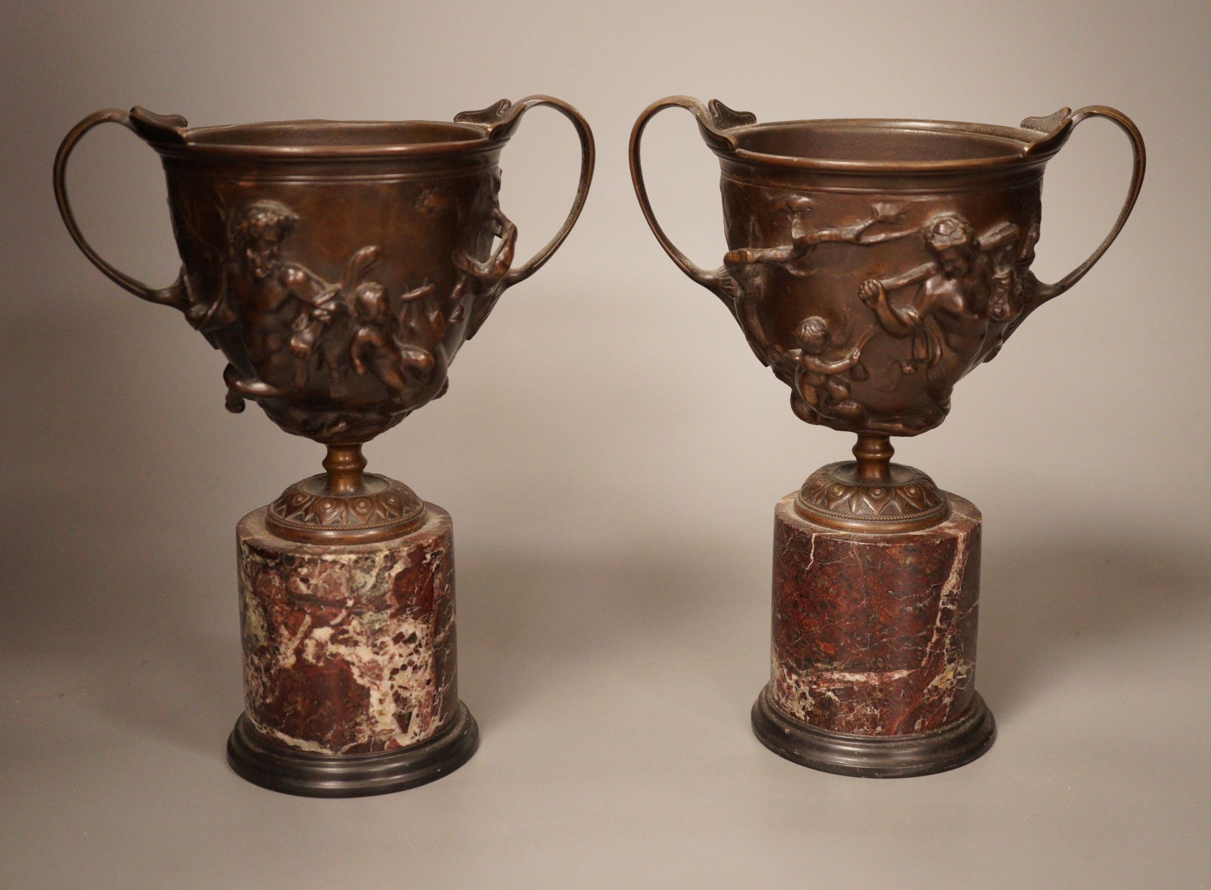 A pair of early 20th century twin handled bronze cups on marble plinth bases, 22cm